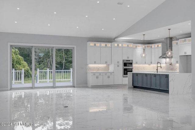 kitchen with lofted ceiling, white cabinetry, stainless steel double oven, wall chimney exhaust hood, and decorative light fixtures