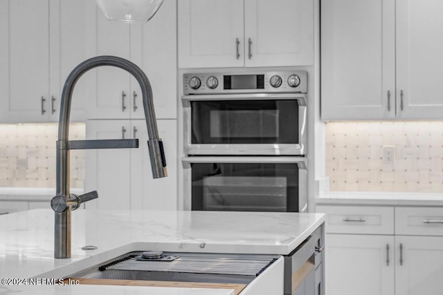 kitchen featuring white cabinetry, double oven, light stone counters, and backsplash