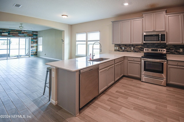 kitchen with light wood-type flooring, sink, kitchen peninsula, appliances with stainless steel finishes, and ceiling fan