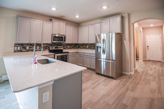 kitchen featuring light hardwood / wood-style floors, sink, gray cabinetry, appliances with stainless steel finishes, and light stone countertops