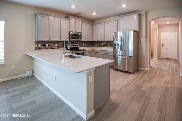 kitchen with appliances with stainless steel finishes, kitchen peninsula, light hardwood / wood-style floors, and sink