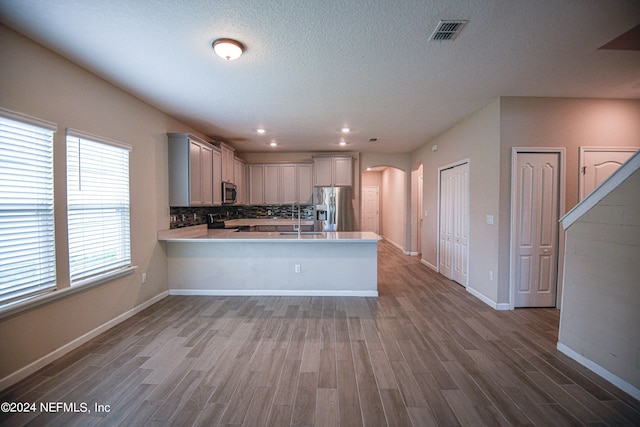 kitchen featuring kitchen peninsula, a textured ceiling, hardwood / wood-style flooring, appliances with stainless steel finishes, and decorative backsplash