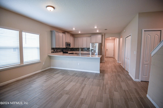 kitchen featuring appliances with stainless steel finishes, light hardwood / wood-style floors, tasteful backsplash, kitchen peninsula, and sink