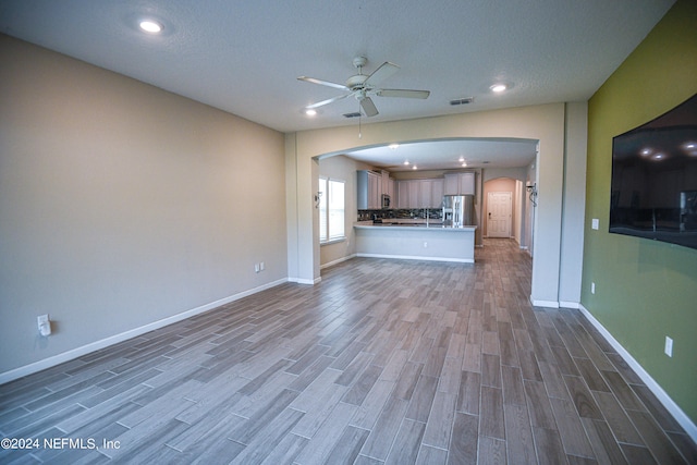 unfurnished living room featuring ceiling fan, hardwood / wood-style flooring, and a textured ceiling