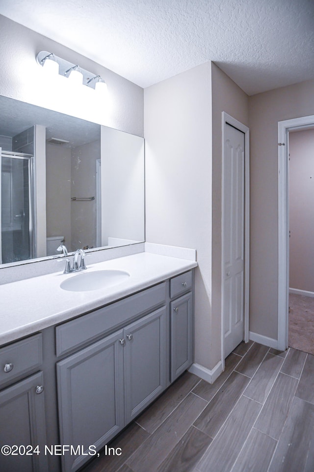 bathroom with walk in shower, a textured ceiling, vanity, and toilet