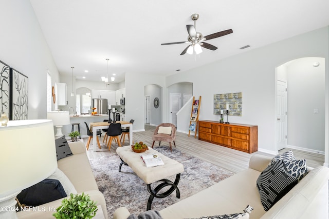 living room with ceiling fan with notable chandelier, light wood-type flooring, and sink