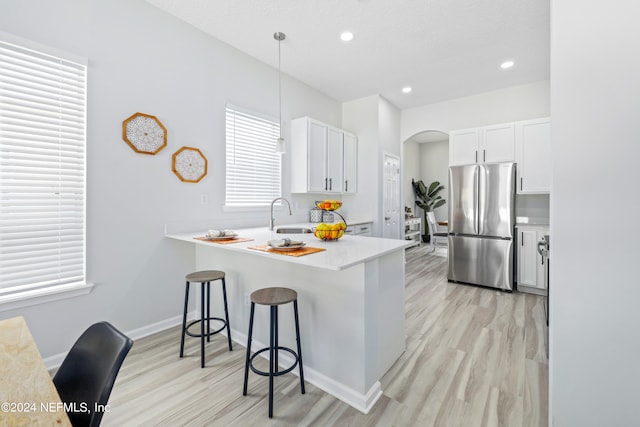 kitchen featuring stainless steel fridge, white cabinetry, a kitchen bar, light hardwood / wood-style flooring, and decorative light fixtures