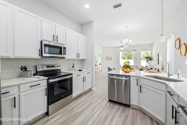 kitchen with pendant lighting, sink, white cabinets, light hardwood / wood-style flooring, and stainless steel appliances