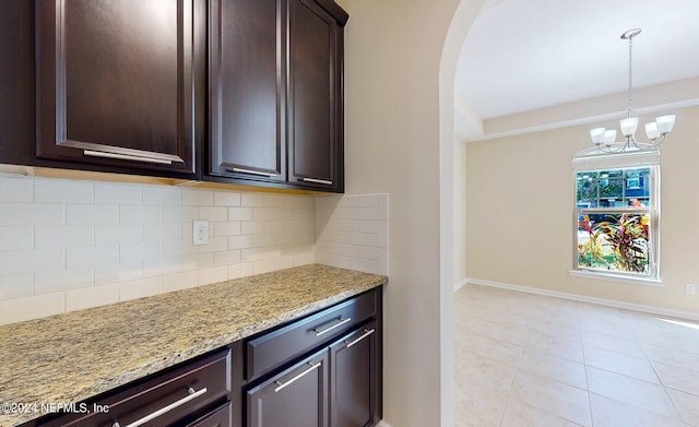 kitchen with decorative backsplash, a chandelier, dark brown cabinetry, and light stone countertops