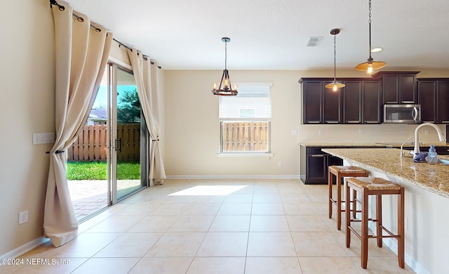 kitchen featuring light stone counters, a breakfast bar area, dark brown cabinets, and a healthy amount of sunlight