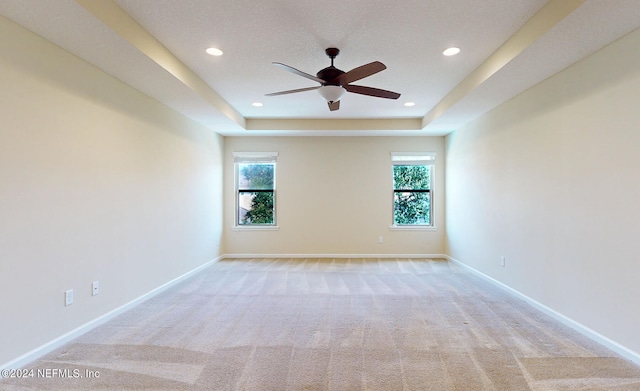 carpeted spare room with ceiling fan, a raised ceiling, and plenty of natural light