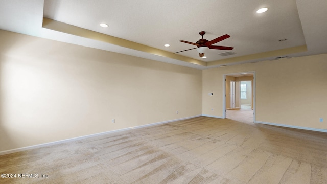 empty room with light carpet, ceiling fan, and a raised ceiling