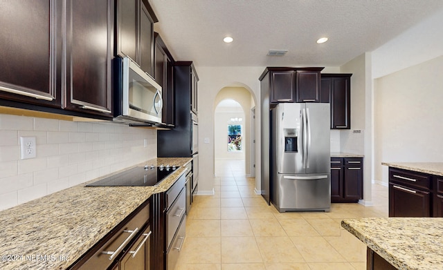 kitchen featuring light stone counters, light tile patterned flooring, decorative backsplash, appliances with stainless steel finishes, and dark brown cabinetry