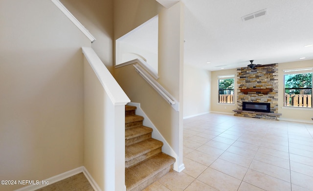 stairs featuring a stone fireplace, ceiling fan, tile patterned floors, and plenty of natural light