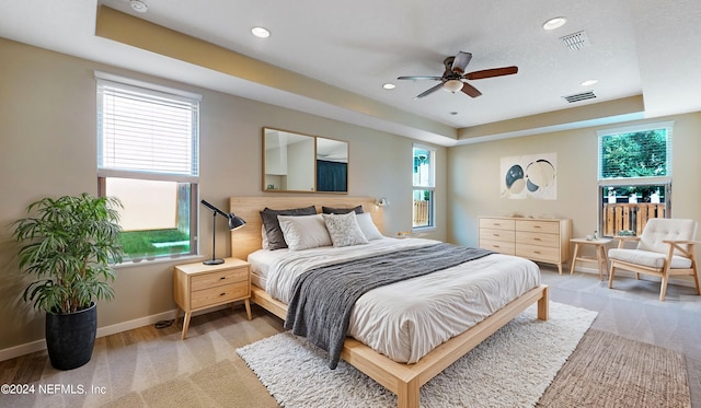 carpeted bedroom featuring ceiling fan, a tray ceiling, and multiple windows