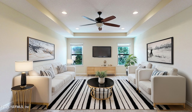 living room with ceiling fan, a raised ceiling, light wood-type flooring, and a wealth of natural light