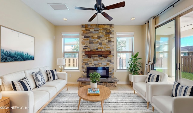 living room with ceiling fan, a stone fireplace, light wood-type flooring, and a healthy amount of sunlight