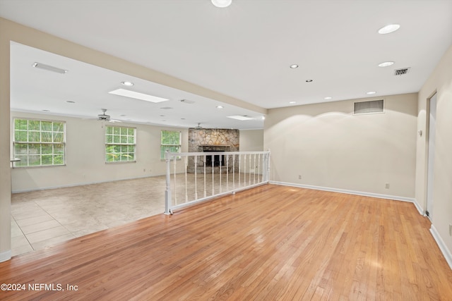 unfurnished living room with ceiling fan, a stone fireplace, and light hardwood / wood-style flooring