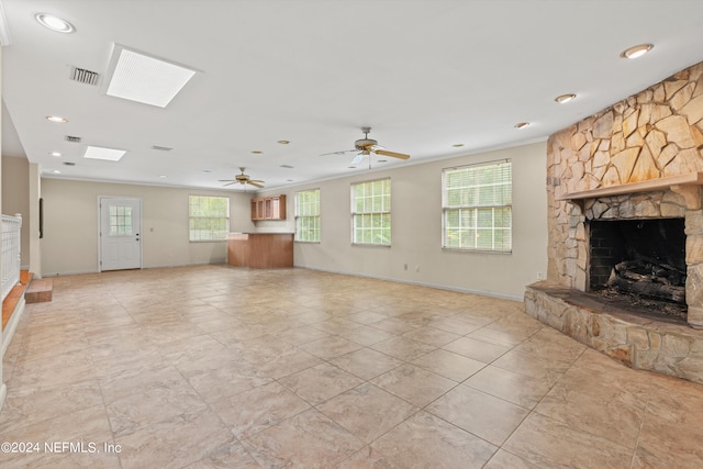 unfurnished living room featuring ceiling fan, a stone fireplace, a skylight, and ornamental molding