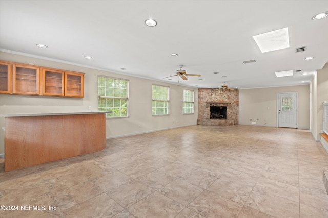 unfurnished living room with ceiling fan, a fireplace, crown molding, and a skylight