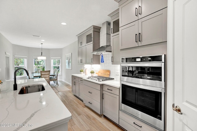 kitchen with appliances with stainless steel finishes, wall chimney exhaust hood, light hardwood / wood-style flooring, decorative light fixtures, and sink