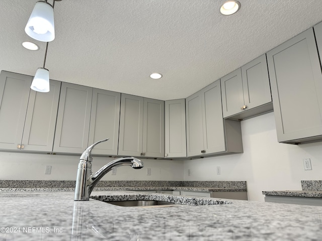 kitchen with gray cabinets, light stone counters, hanging light fixtures, and sink