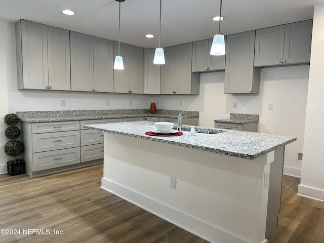 kitchen featuring sink, light stone counters, dark hardwood / wood-style flooring, gray cabinets, and a kitchen island with sink