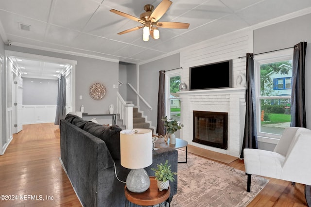 living room featuring a brick fireplace, wood-type flooring, and a healthy amount of sunlight