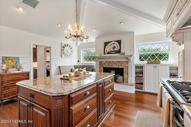 kitchen with hanging light fixtures, dark wood-type flooring, a center island, an inviting chandelier, and light stone countertops