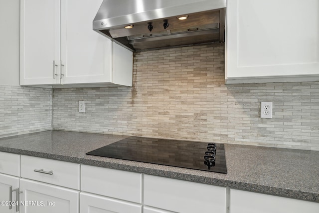 kitchen featuring backsplash, wall chimney exhaust hood, black electric cooktop, and white cabinets