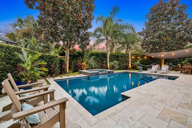 pool at dusk featuring a patio and an in ground hot tub