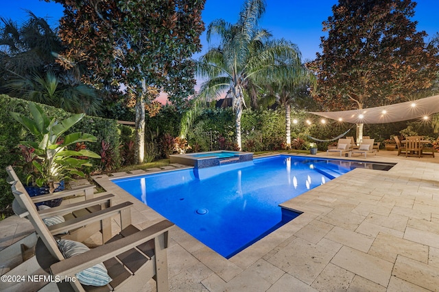 pool at dusk with an in ground hot tub and a patio