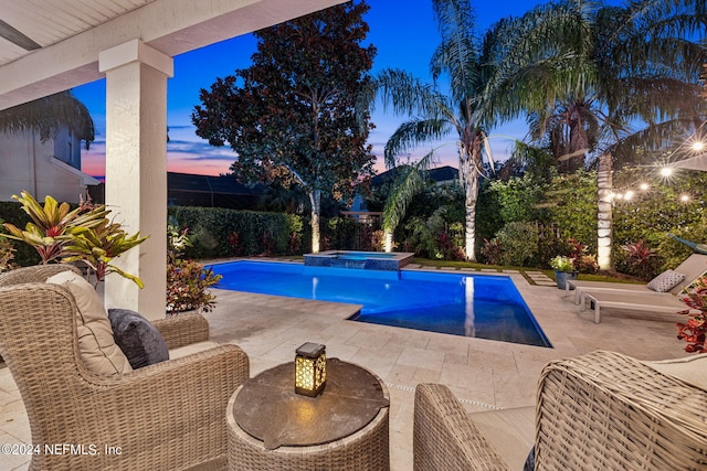 pool at dusk with a patio area, pool water feature, and an in ground hot tub