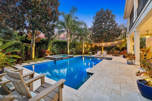 pool at dusk with an in ground hot tub and a patio