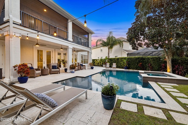 pool at dusk with french doors, an in ground hot tub, an outdoor living space, a lanai, and a patio area