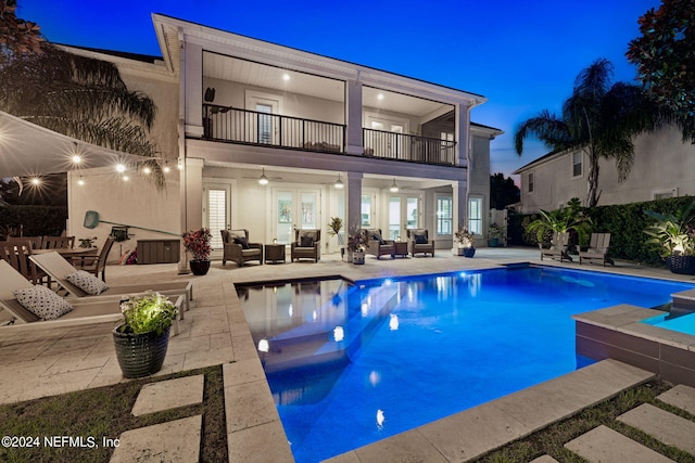 back house at dusk with a balcony, an outdoor hangout area, a patio, and a pool with hot tub