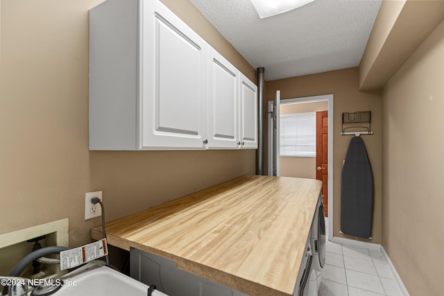 clothes washing area with cabinets, a textured ceiling, electric dryer hookup, and light tile patterned floors