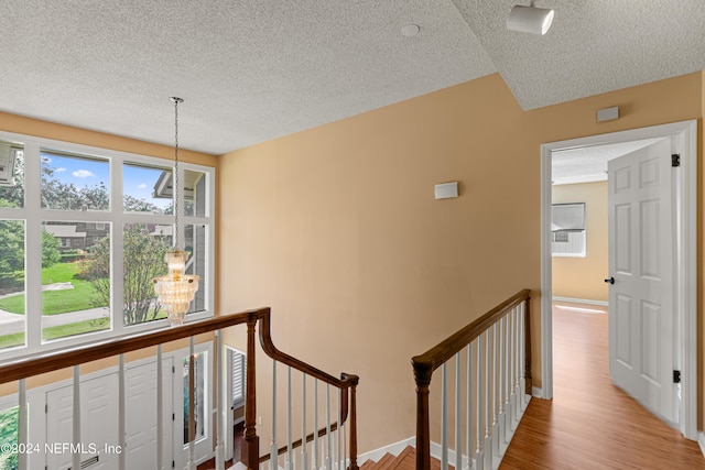 corridor featuring an inviting chandelier, a textured ceiling, and light hardwood / wood-style floors