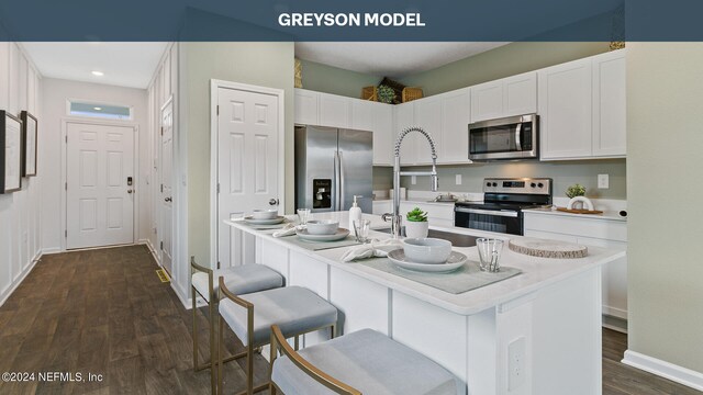 kitchen with appliances with stainless steel finishes, a breakfast bar area, white cabinetry, and dark hardwood / wood-style floors