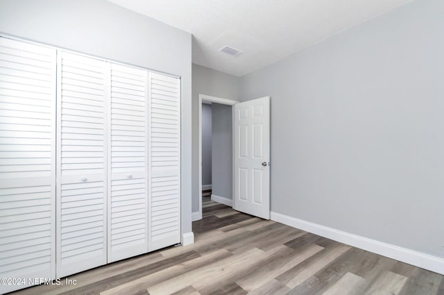 unfurnished bedroom featuring light wood-type flooring, a closet, and a textured ceiling