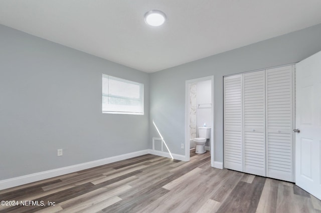 unfurnished bedroom featuring wood-type flooring, connected bathroom, and a closet