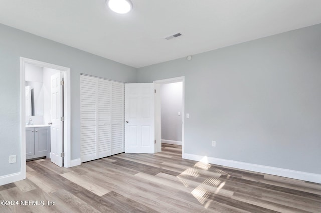 unfurnished bedroom with light wood-type flooring, ensuite bath, and a closet