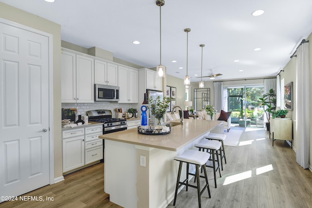 kitchen featuring hanging light fixtures, white cabinetry, an island with sink, stainless steel appliances, and a kitchen bar