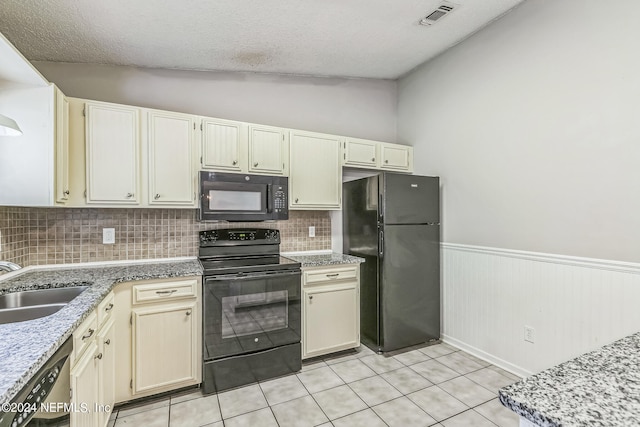 kitchen featuring cream cabinetry, vaulted ceiling, and black appliances