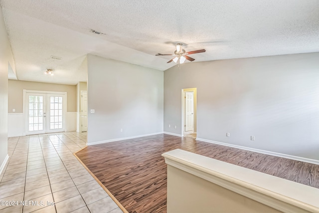 unfurnished room featuring a textured ceiling, lofted ceiling, ceiling fan, light hardwood / wood-style flooring, and french doors