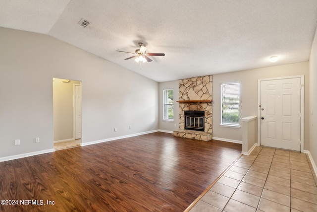 unfurnished living room with a textured ceiling, a stone fireplace, vaulted ceiling, and light hardwood / wood-style flooring