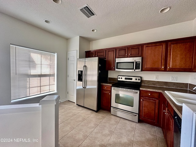 kitchen with appliances with stainless steel finishes, a textured ceiling, sink, and light tile patterned floors