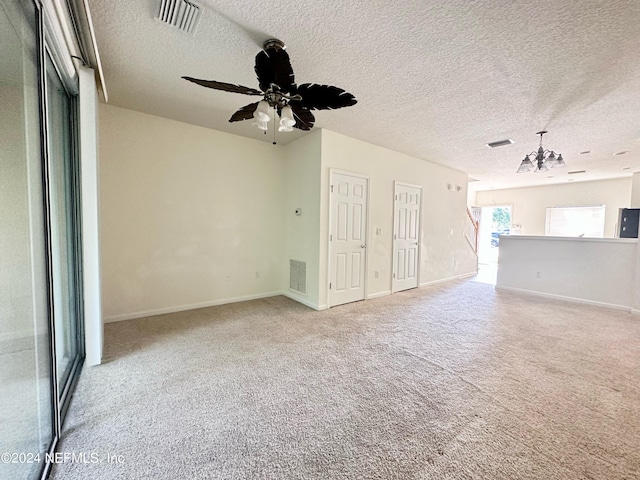 unfurnished living room with a textured ceiling, ceiling fan with notable chandelier, and light carpet