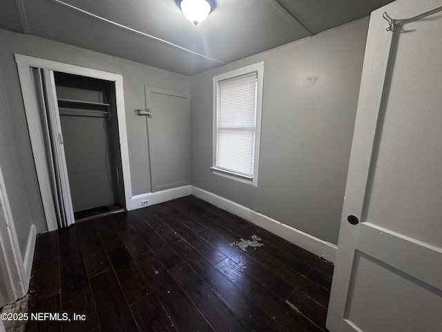 unfurnished bedroom featuring a closet, baseboards, and dark wood-type flooring