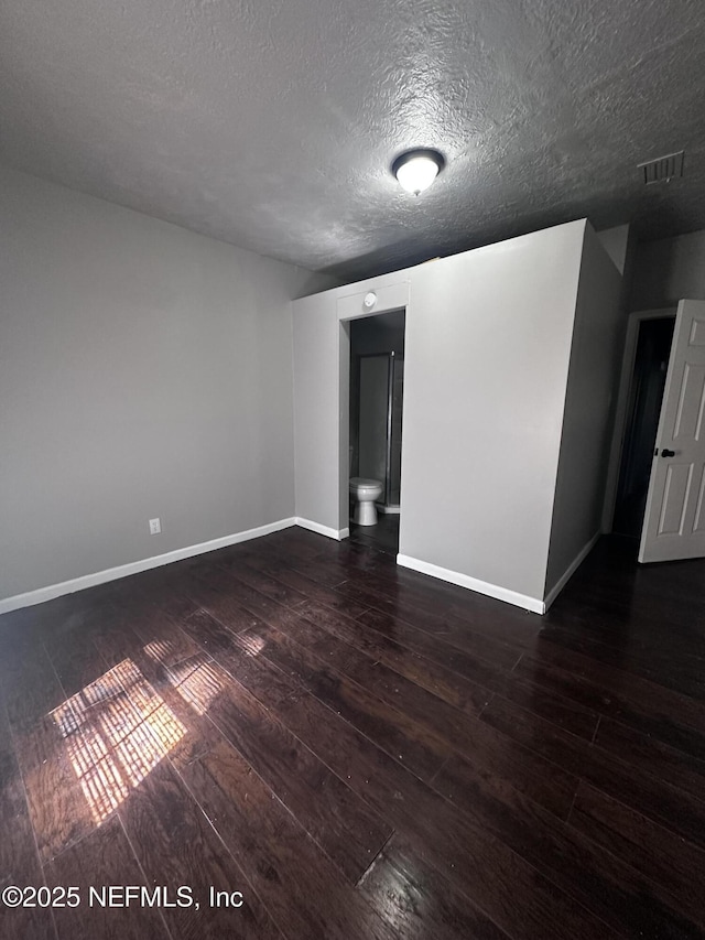 empty room with dark wood-style floors, a textured ceiling, visible vents, and baseboards